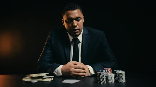 African American man feeling disappointed while checking his poker cards, loss