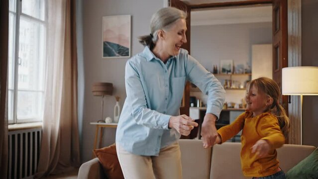 Authentic portrait of a cheerful senior woman, grandmother dancing with her lovely granddaughter