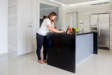 A beautiful woman smiles as she works on her laptop at a table in her kitchen at home