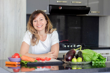 Beautiful young woman cooks food happy at the table in a modern kitchen on gray background