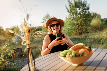 Happy Woman freelancer use phone and drinking cocktail call while relaxing on cozy glamping tent in sunny day. Luxury camping tent for outdoor summer holiday and vacation. Lifestyle concept