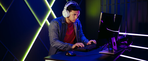 Fototapeta na wymiar Young man playing an online video game on a pc, with a headset for communication with other gamers