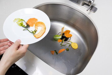 Woman trowing away food scraps in the kitchen sink