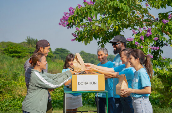 volunteers giving paper bag of food to asian senior woman and son,group of volunteers helping the needy to distribute of food items and water in the rural park