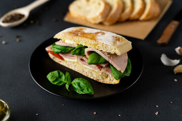 Ciabatta Sandwich with Ham, Pesto sauce, Tomatoes, Basil on a black background. Food. Food background