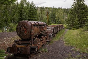 Old rusty train - steam locomotive. An abandoned coal mine overgrown with forest in the mountains....