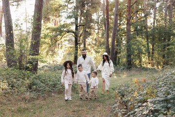 Fototapeta premium Young mother, father with daughter and sons are walking, having fun in autumn forest. Family holding hands enjoying time together at background of trees. Happy parenthood and childhood concept.