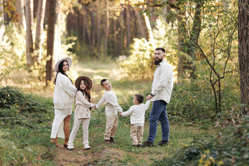 Fototapeta premium Portrait of big family outdoors. Young Stylish bearded dad with little son on shoulder, beautiful brunette mom, child boy and daughter in autumn park, smiling and looking at camera. Happy family day