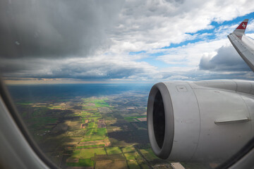 Commercial airplane flying over agricultural fields and meadows. Visible jet engine, and clouds, no people