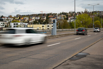 Road traffic speed trap camera in a gray box between 4 lanes of road in a major European city. Blurred traffic, slow shutter speed, no people