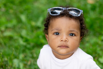 portrait of an African-American baby boy on a green grass lawn in summer wearing sunglasses