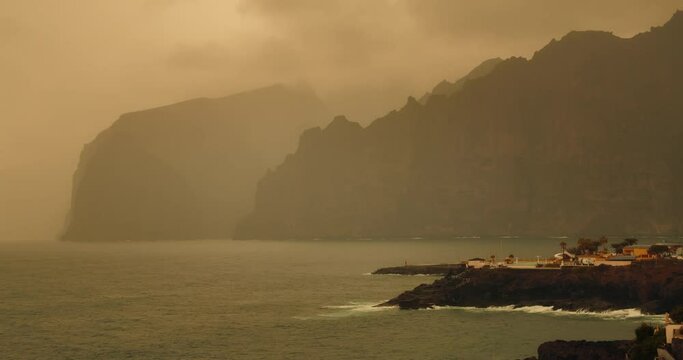 Foggy yellow haze veil covered rocks in the oceam. Sandstorm Calima in Tenerife Los Gigantes. Canary Islands hit by African Sahara dust sand storm. Spain.
