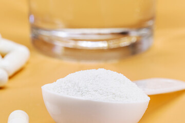 spoon of hydrolyzed collagen powder, and pills, with glass of water, protein for skin elasticity, isolated background and copyspace, macrophotography