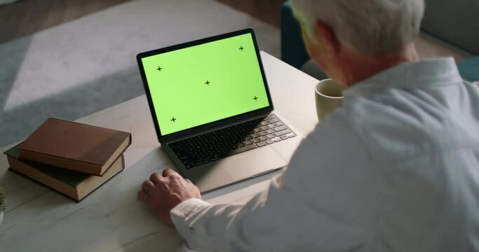Solid old adult male businessman of advanced age at laptop with green screen with tracking markers. Working from home, male remote worker at laptop with green screen. Senior male worker at laptop.