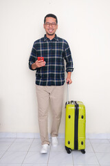 Full body portrait of man smiling and walking towards camera holding luggage and phone