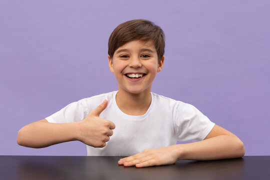 Happy schoolboys sitting at desk, classroom. Shows a thumbs up. Violet background