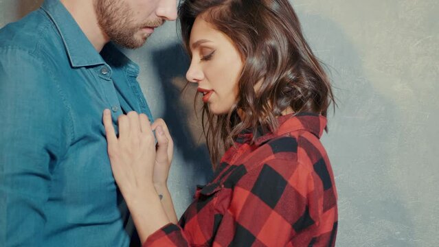 Hot beautiful woman and her handsome boyfriend. Models posing near grey wall in jeans clothes. Young passionate couple hugging. Sensual pair getting closer for kiss. Lover couple