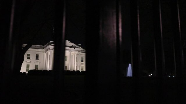 Wide angle motion to the right of the US Presidents home, the White House in Washington, DC. View through the iron bars in front on the South side at night.