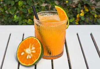 Orange juice with ice on white wooden table with slice of orange and copy space