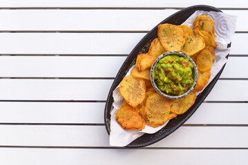 Homemade potato chips with vegetarian sauce made of avocado and vegetables on white wooden table