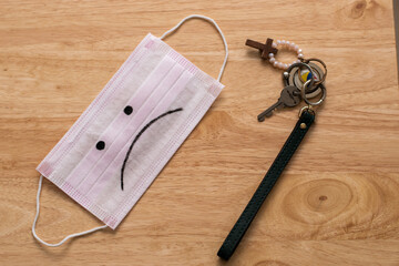 A mask with a sad face drawn and a house key over a table of wood