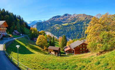 Fototapeta na wymiar Autumn panoramic mountain view with chalet on the meadow in the valley near Swiss alpine village Wengen.