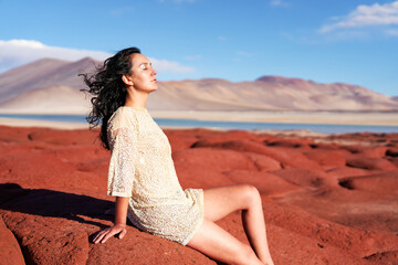 Fototapeta na wymiar portrait beautiful young woman sitting relaxed in the Salar de Aguas Calientes on red stones breathing the desert air of the altiplano