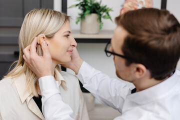 A young attractive otolaryngologist doctor gives a consultation to a female patient. A doctor explains how to wear a hearing aid to a woman - obrazy, fototapety, plakaty