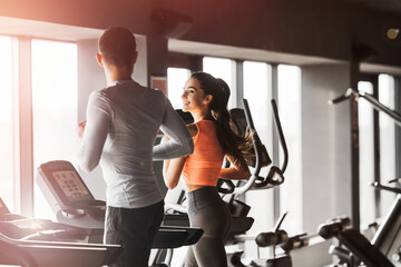 Fit happy couple running together on treadmills at the gym. Girl smiling boyfriend. Copy space. Back view.