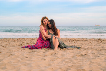 Pensive girlfriends sitting on sandy beach