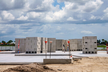Many hollow concrete blocks for masonry walls, arranged in multiple stacks on new foundation of single-family house under construction, in a suburban lakeside development on a cloudy day in Florida