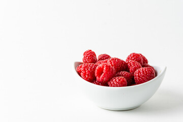Top view of white bowl with red raspberries, horizontal white background with copy space