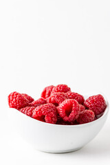 Top view of white bowl with red raspberries, selective focus, on white background in vertical with copy space