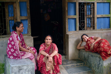 South asian village women gossiping and passing leisure time wearing red traditional dress and sitting outside the door 