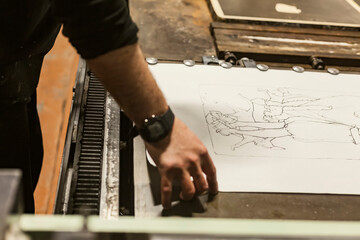 The artist is placing a paper stencil or template on a lithographic press or rolling press used for...
