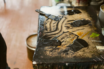 The artist is mixing paint and chemicals with a spatulas in a Lithographic art workshop.