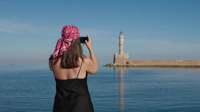 Woman tourist taking pictures and enjoying near lighthouse of Chania In Crete, Greece. 
