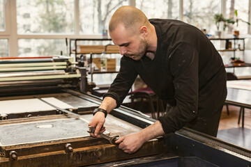 The artist is tightening nuts in the lithographic press or rolling press.