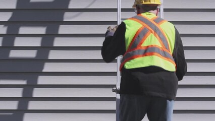 Industrial worker climbing a ladder in front of exterior siding
