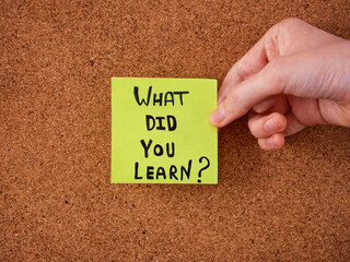 A young man holding a green sticky note with the question what did you learn written on it