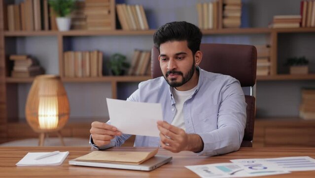 indian male opening envelope and reading fortunate news in a mail letter. feeling happy about job approval or exam results