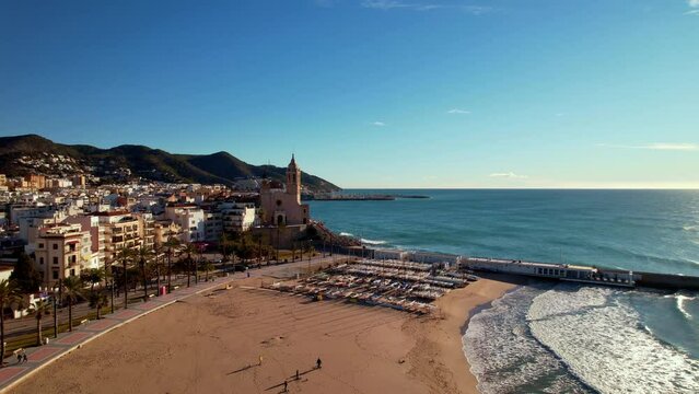 Panoramic aerial drone view of coastal village, Sant Bartomeu i Santa Tecla de Sitges during sunny day in Sitges, town near Barcelona in Catalonia, Spain. It is famous for its beaches and nightlife