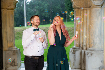 Stylish man in a suit and a young lady in a fashionable green dress blowing bubbles - Powered by Adobe