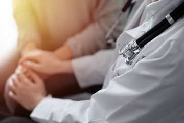Doctor and patient sitting at green sofa. The focus is on female physician's hands reassuring woman, close up. Medicine concept