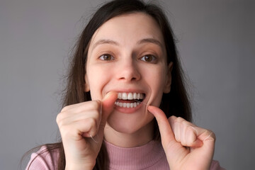 Portrait of young woman is cleaning her white teeth with dental floss smiling in bathroom. Everyday...