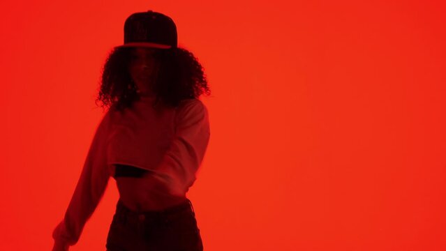 Fashion woman dancing in RnB style. The black young model moves rhythmically. Female dancer posing on red neon background in studio. Hip hop and breakdance technique