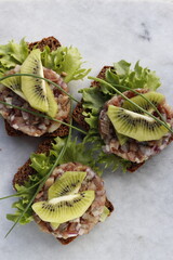 Three slices of rye bread with herring tartare, garnished with kiwi slices.