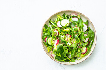 Green salad with spinach, arugula and radish with olive oil on white table. Top view with copy space.