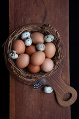 Wicker basket with chicken and quail eggs on a wooden board.