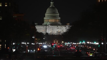 Long lens view of the West side of the US Capitol building at night showing scaffolding for repairs and construction from Pennsylvania Avenue with traffic, in Washington DC